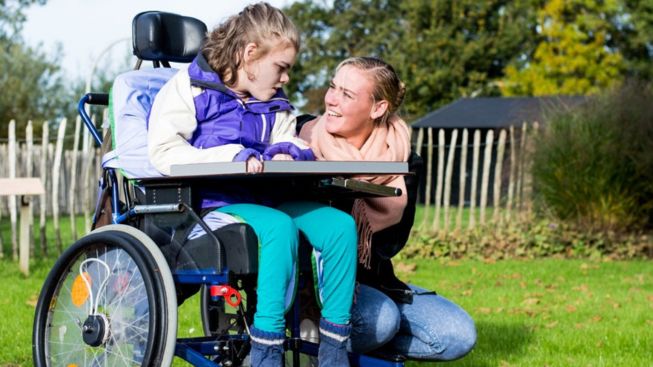 Gehandicapt meisje in rolstoel met verzorger